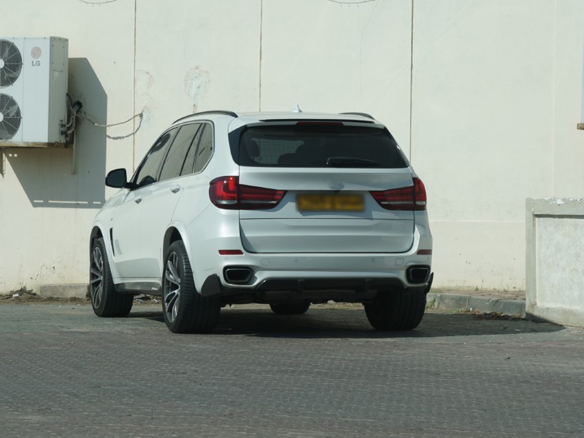 A white luxury SUV, parked next to a white wall.