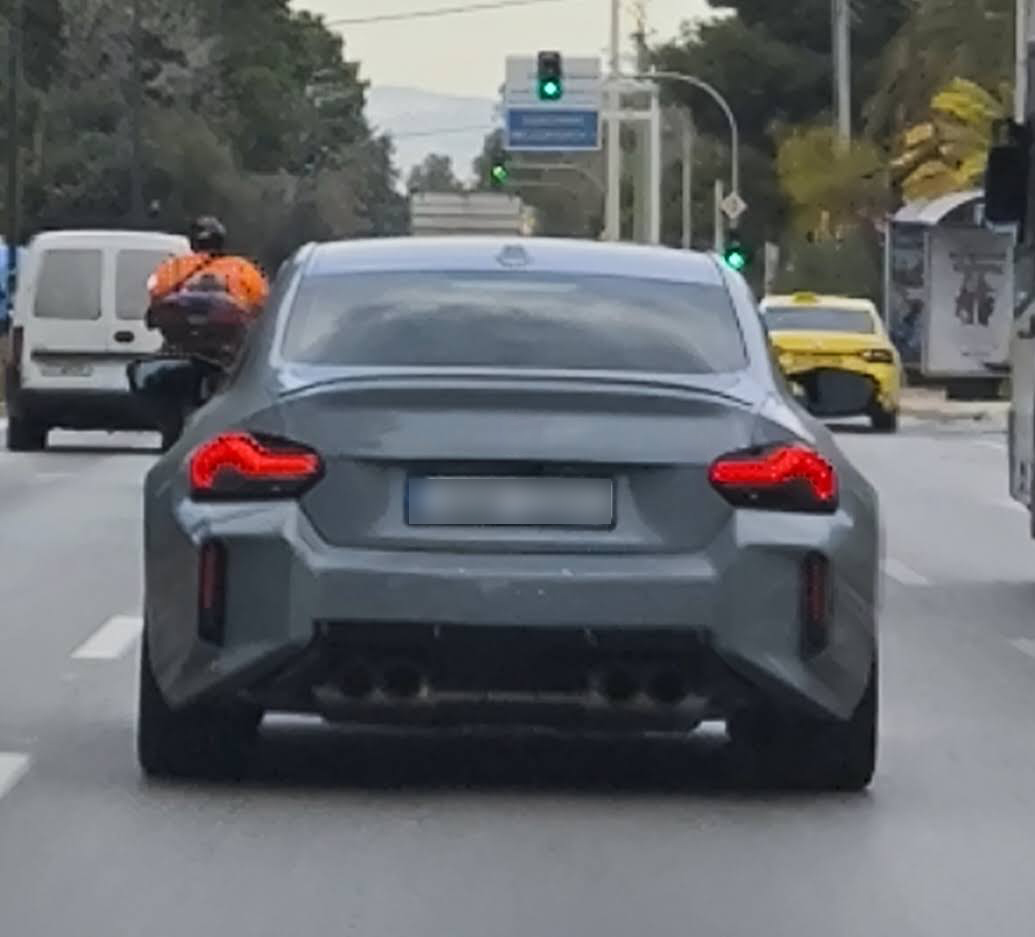 The rear view of a gray sedan, driving in city traffic.