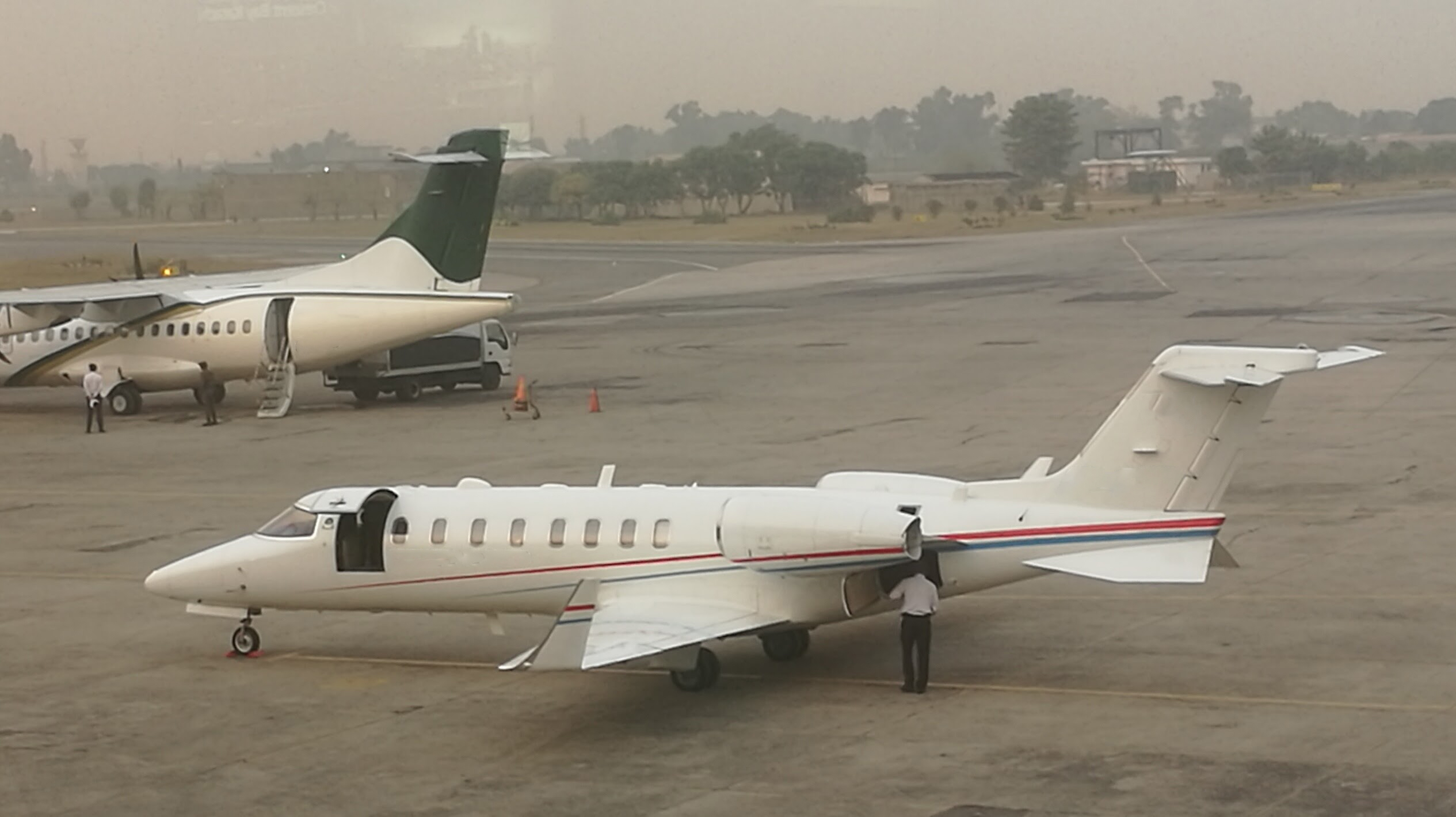 A white private jet with red and blue stripes parked on a runway.