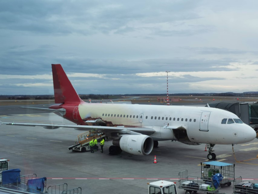 A medium-sized passenger aircraft with a red tail parked at an airport gate.