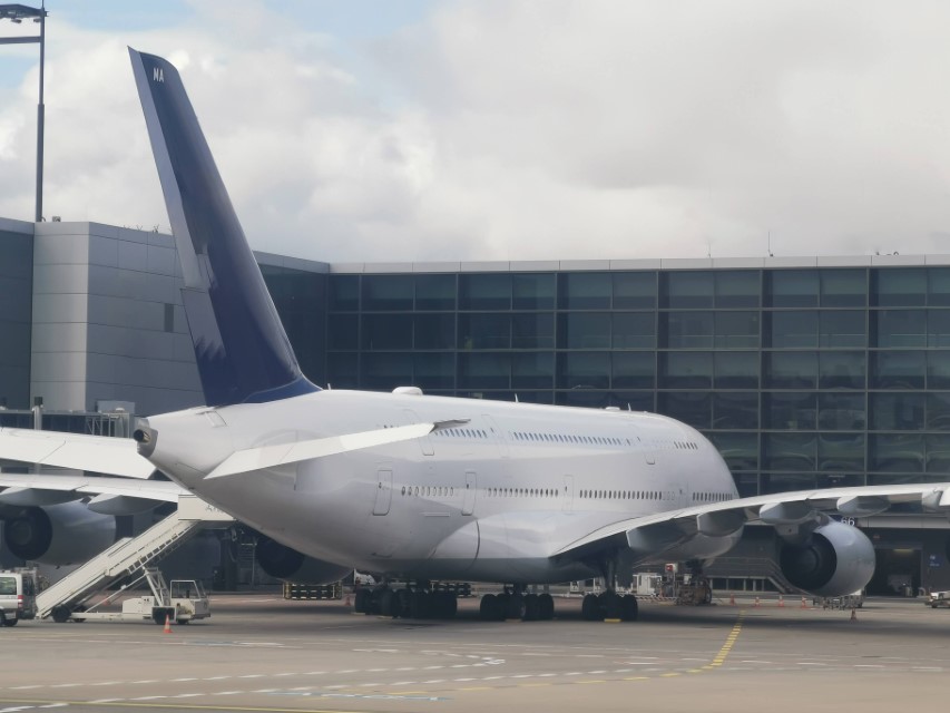 A large white passenger airplane with a blue tail docked at a modern airport terminal.