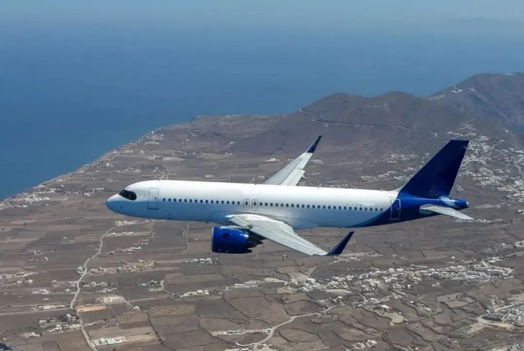 A commercial jet flying over a coastal landscape.