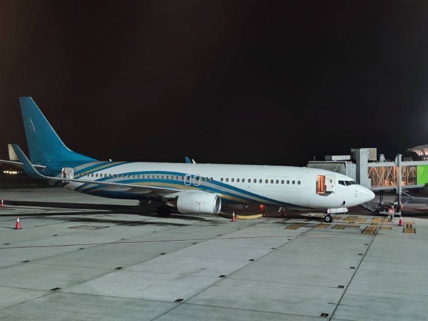 A white passenger airplane with blue stripes connected to a boarding bridge.