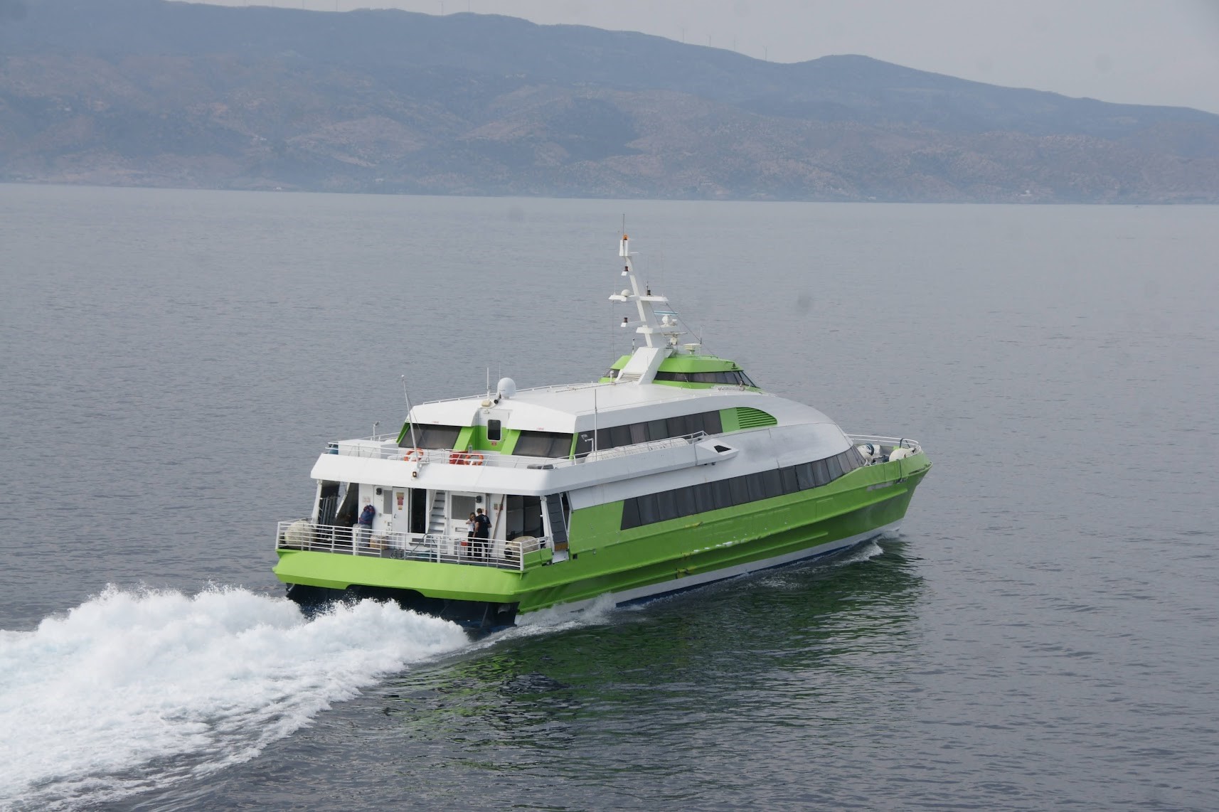 A green and white ferry cruising through the water at high speed.