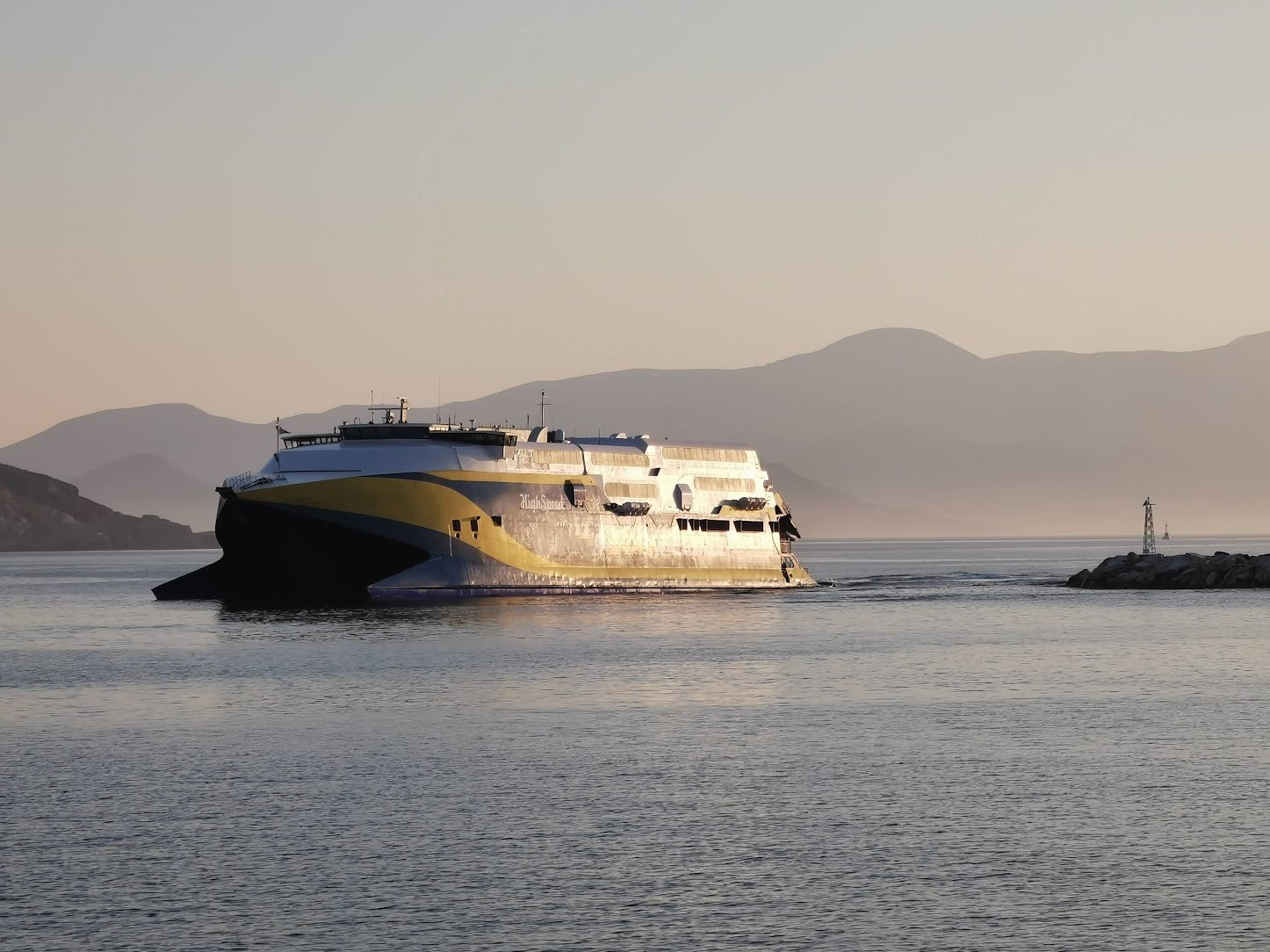 A yellow and blue catamaran ferry departing from a port.