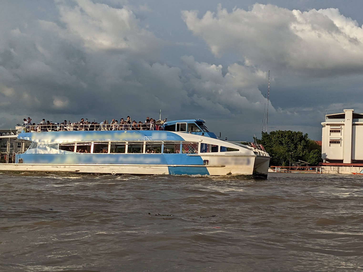 A crowded riverboat ferry with a blue and white design.